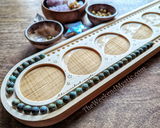 Close-up of African turquoise beads being counted on wood mala board, sitting with crystals and bowls of beading supplies.