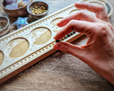 Hand holding a bead about to be placed in mala design board, surrounded by bowls of beads and crystals.